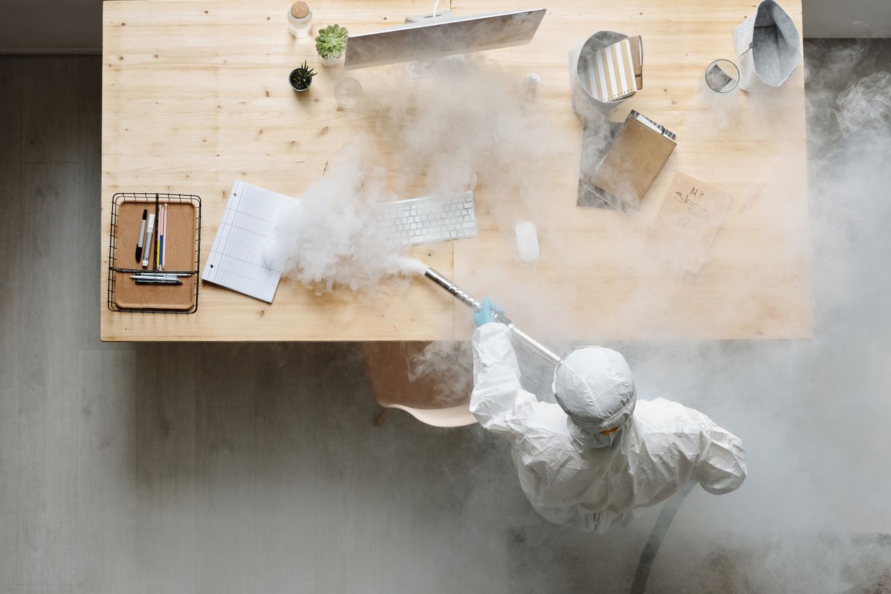 team-01 An individual disinfects a workspace using fumigation, wearing full protective gear for safety.